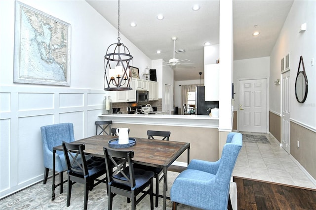 dining space with vaulted ceiling, ceiling fan with notable chandelier, and light hardwood / wood-style flooring