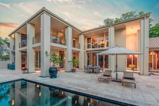 back house at dusk with a balcony and a patio area