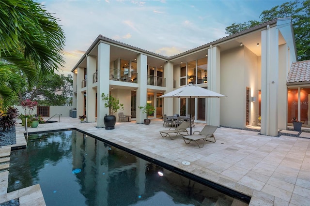 back house at dusk with a balcony and a patio area