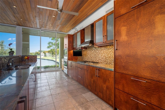 kitchen featuring sink, dark stone counters, stainless steel gas cooktop, wood ceiling, and wall chimney exhaust hood