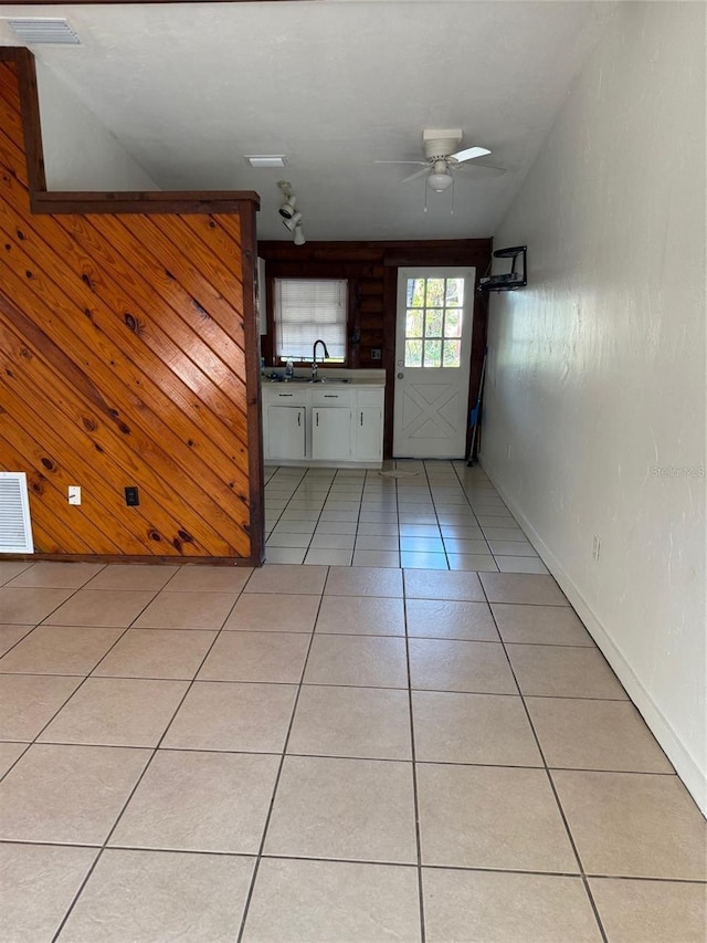 interior space featuring light tile patterned flooring, ceiling fan, wooden walls, and sink