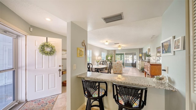 kitchen featuring light stone countertops, kitchen peninsula, a textured ceiling, and a kitchen bar