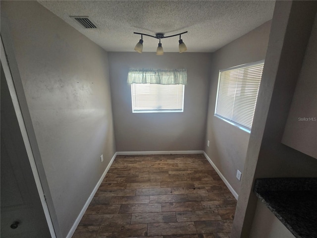 unfurnished dining area featuring track lighting, a healthy amount of sunlight, dark hardwood / wood-style flooring, and a textured ceiling