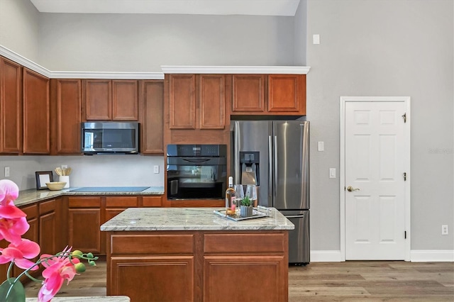 kitchen featuring a kitchen island, light wood-type flooring, light stone counters, and black appliances