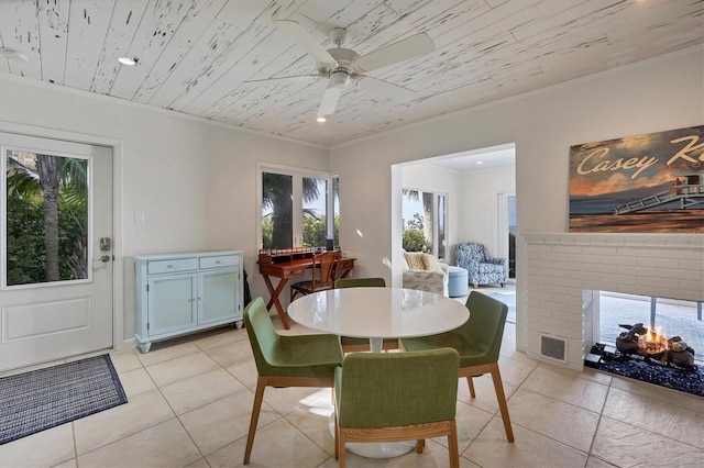 tiled dining room with a brick fireplace, ornamental molding, wooden ceiling, and ceiling fan