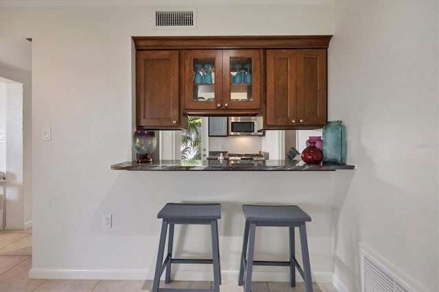 kitchen with a kitchen bar, kitchen peninsula, light tile patterned floors, and dark stone countertops