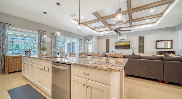 kitchen with coffered ceiling, sink, light stone counters, a center island with sink, and dishwasher