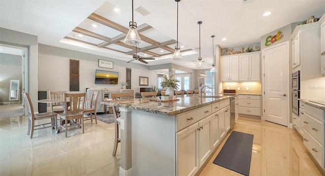 kitchen with coffered ceiling, sink, a large island with sink, a kitchen breakfast bar, and pendant lighting