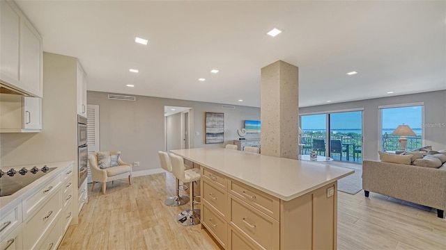 kitchen featuring light wood-type flooring, a center island, black electric cooktop, and a breakfast bar