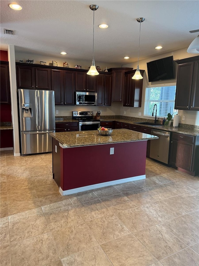 kitchen with hanging light fixtures, appliances with stainless steel finishes, a center island, and sink