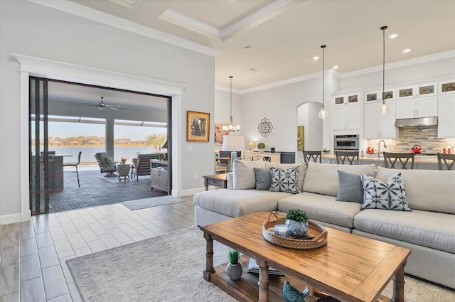 living room with ornamental molding, a water view, sink, and ceiling fan with notable chandelier