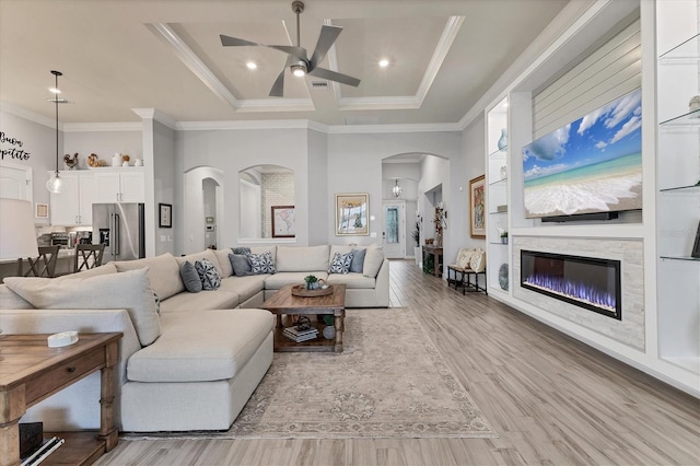 living room with crown molding, a towering ceiling, ceiling fan, and light hardwood / wood-style flooring