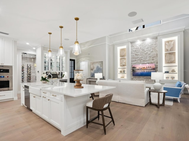 kitchen with decorative light fixtures, an island with sink, sink, white cabinets, and light hardwood / wood-style floors