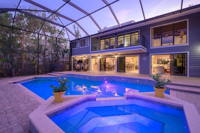 pool at dusk featuring an in ground hot tub, a patio area, and glass enclosure