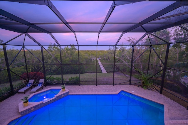 pool at dusk with an in ground hot tub, a patio area, and glass enclosure