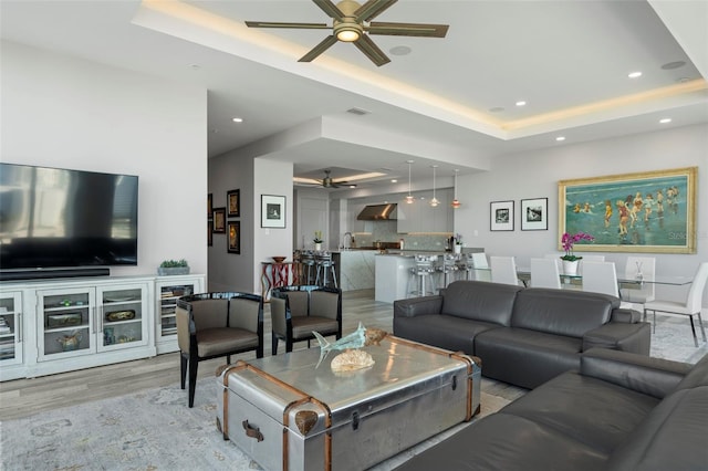 living room featuring light hardwood / wood-style floors, ceiling fan, and a tray ceiling