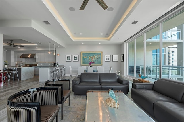 living room featuring light hardwood / wood-style floors, ceiling fan, and a tray ceiling