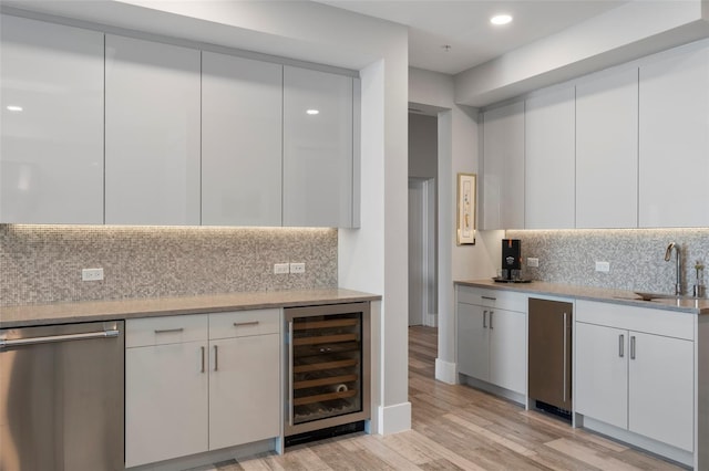 kitchen featuring wine cooler, sink, light wood-type flooring, stainless steel dishwasher, and white cabinets