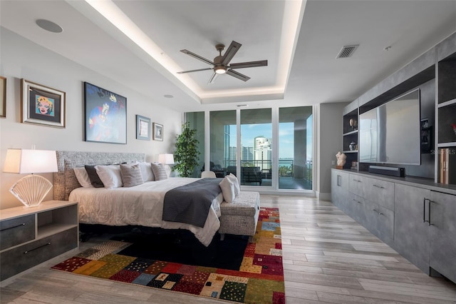 bedroom featuring light hardwood / wood-style flooring, ceiling fan, access to exterior, floor to ceiling windows, and a raised ceiling