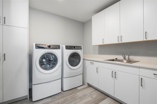 clothes washing area featuring light hardwood / wood-style floors, sink, cabinets, and washer and dryer