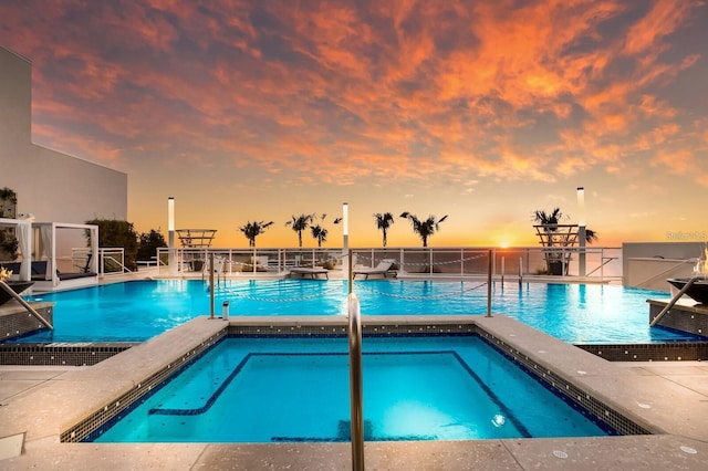 pool at dusk featuring a hot tub