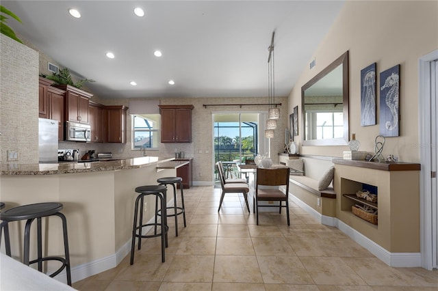 kitchen featuring pendant lighting, a breakfast bar, appliances with stainless steel finishes, light stone counters, and kitchen peninsula