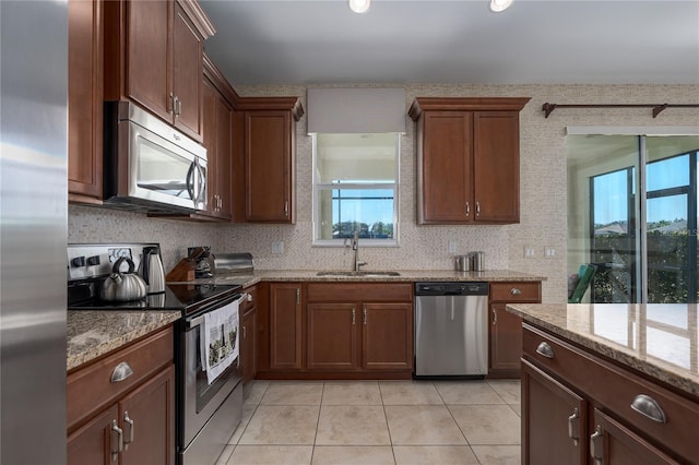 kitchen featuring sink, light tile patterned floors, stainless steel appliances, light stone countertops, and backsplash