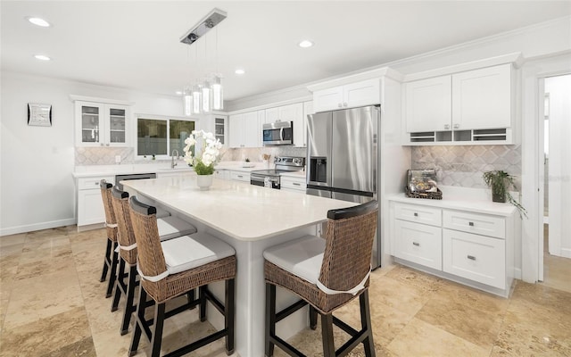 kitchen with appliances with stainless steel finishes, white cabinetry, a kitchen breakfast bar, hanging light fixtures, and a center island