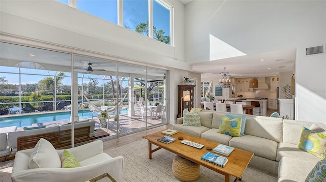 living room featuring a towering ceiling, ceiling fan with notable chandelier, and light hardwood / wood-style floors