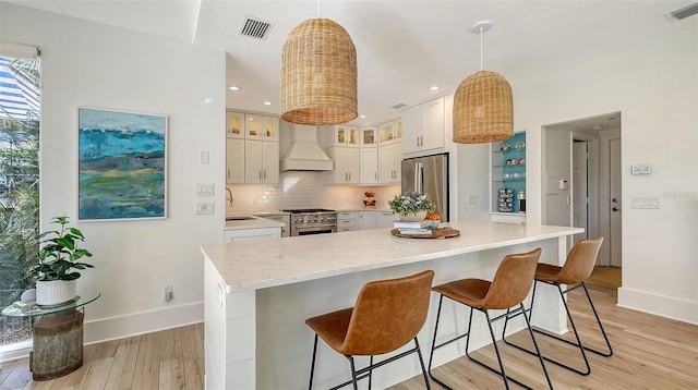 kitchen featuring pendant lighting, appliances with stainless steel finishes, light stone counters, and custom exhaust hood