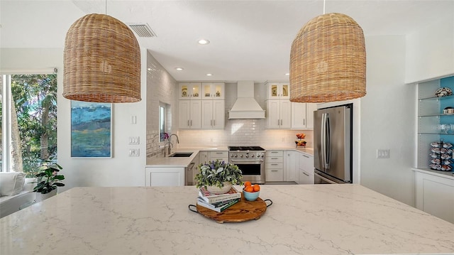 kitchen featuring white cabinetry, light stone counters, appliances with stainless steel finishes, custom range hood, and decorative backsplash