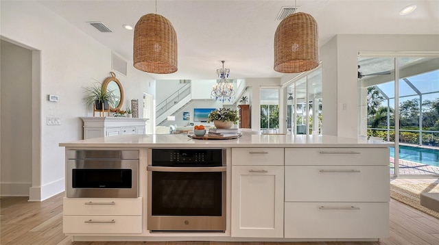 kitchen with hanging light fixtures, white cabinetry, a healthy amount of sunlight, and oven