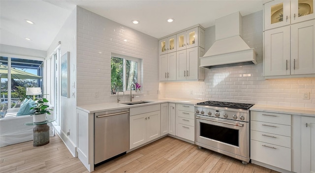 kitchen featuring appliances with stainless steel finishes, sink, white cabinets, custom exhaust hood, and light hardwood / wood-style flooring