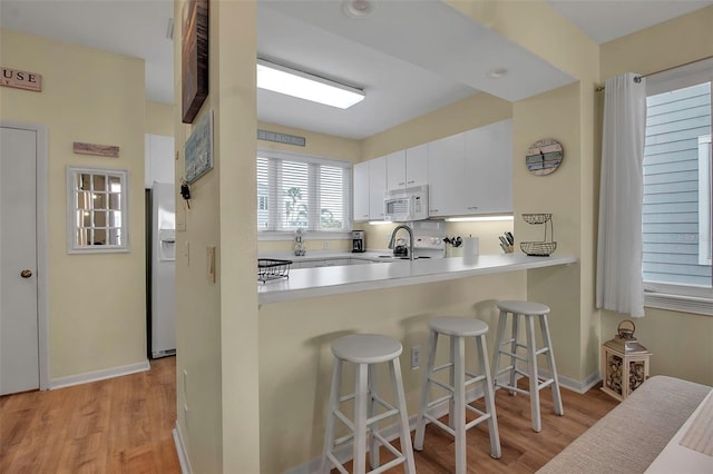 kitchen featuring white cabinetry, a kitchen bar, kitchen peninsula, white appliances, and light hardwood / wood-style flooring