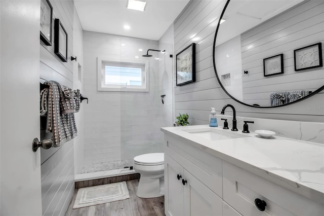 bathroom with tiled shower, toilet, wood walls, wood-type flooring, and vanity