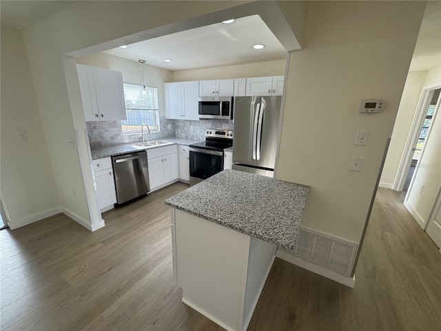 kitchen with pendant lighting, white cabinets, a center island, light stone counters, and stainless steel appliances