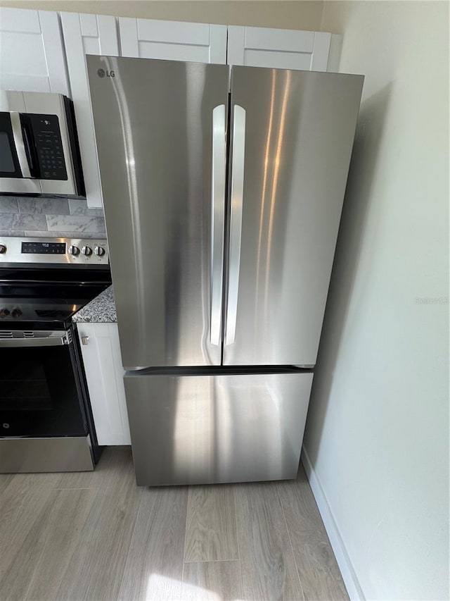 kitchen featuring appliances with stainless steel finishes, backsplash, white cabinets, light stone counters, and light hardwood / wood-style floors