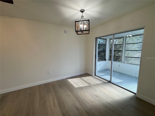 empty room with wood-type flooring and a chandelier