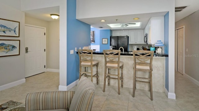 kitchen featuring a breakfast bar area, a skylight, a tray ceiling, black appliances, and white cabinets