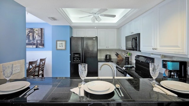 kitchen with a raised ceiling, white cabinetry, ornamental molding, and black appliances