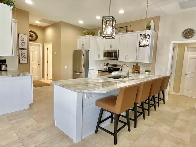 kitchen with sink, appliances with stainless steel finishes, kitchen peninsula, pendant lighting, and light stone countertops