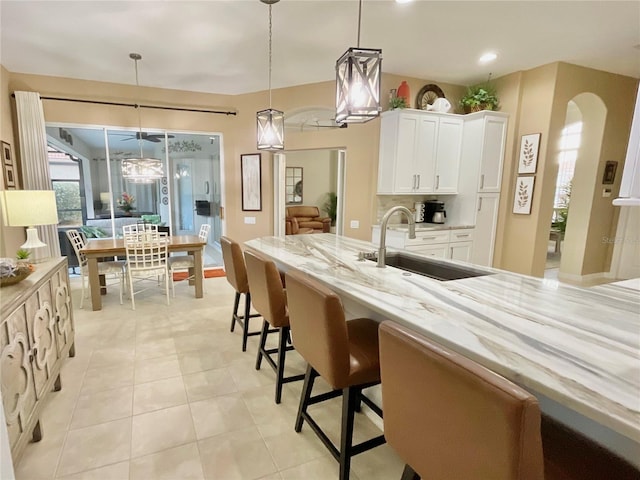 kitchen with decorative light fixtures, white cabinetry, sink, a kitchen bar, and light stone countertops