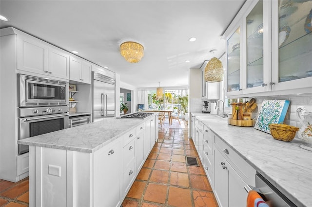 kitchen featuring tasteful backsplash, built in appliances, a kitchen island, light stone countertops, and white cabinets