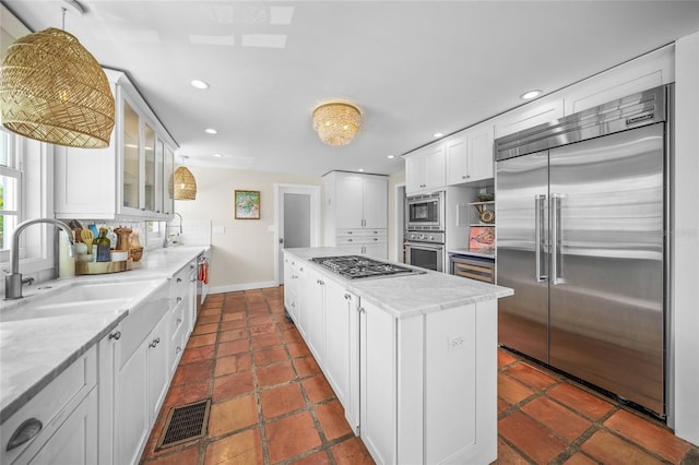 kitchen with tasteful backsplash, sink, white cabinets, a center island, and built in appliances