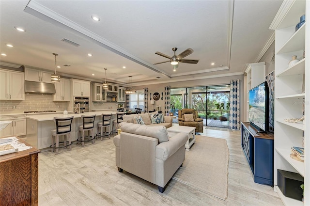 living room with ornamental molding, light hardwood / wood-style floors, ceiling fan, and a tray ceiling