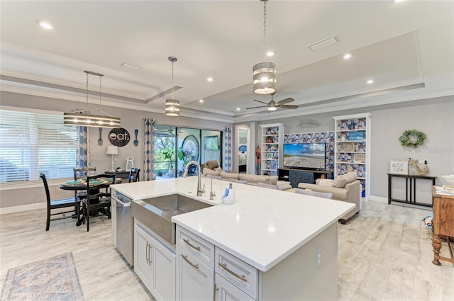 kitchen featuring pendant lighting, sink, an island with sink, stainless steel dishwasher, and a raised ceiling