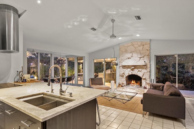 kitchen featuring light tile patterned flooring, a stone fireplace, lofted ceiling, sink, and ceiling fan