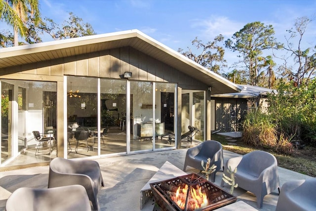 rear view of property featuring a sunroom, a patio, and an outdoor fire pit