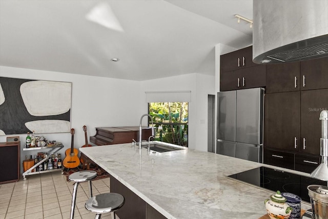 kitchen featuring lofted ceiling, sink, a breakfast bar area, light tile patterned floors, and stainless steel refrigerator