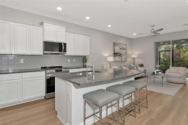 kitchen featuring sink, white cabinetry, a kitchen island with sink, stainless steel appliances, and dark stone counters